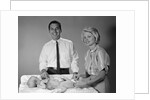 1960s smiling mother and father with twin babies on diaper changing table looking at camera by Anonymous