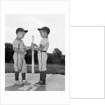 1960s two boys in baseball uniforms choosing sides by getting the upper hand on a bat by Anonymous