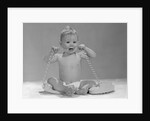 1960s blond baby sitting up looking at camera chewing on telephone cord by Anonymous