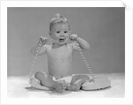 1960s blond baby sitting up looking at camera chewing on telephone cord by Anonymous