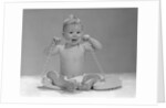 1960s blond baby sitting up looking at camera chewing on telephone cord by Anonymous