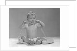 1960s blond baby sitting up looking at camera chewing on telephone cord by Anonymous