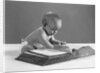 1960s baby wearing glasses looking for a word in big dictionary by Anonymous