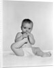 1950s 1960s baby seated on blanket bringing foot to mouth by Anonymous