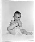 1950s 1960s baby seated on blanket bringing foot to mouth by Anonymous
