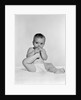 1950s 1960s baby seated on blanket bringing foot to mouth by Anonymous