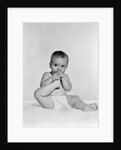 1950s 1960s baby seated on blanket bringing foot to mouth by Anonymous