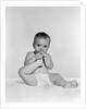 1950s 1960s baby seated on blanket bringing foot to mouth by Anonymous