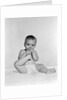 1950s 1960s baby seated on blanket bringing foot to mouth by Anonymous