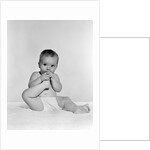 1950s 1960s baby seated on blanket bringing foot to mouth by Anonymous