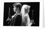 1980s bride and groom standing back to back holding dueling pistols by Anonymous
