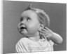 1940s 1950s close-up portrait of baby girl with curl on top of head looking to side with hand held up beside ear by Anonymous