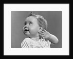 1940s 1950s close-up portrait of baby girl with curl on top of head looking to side with hand held up beside ear by Anonymous