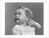 1940s 1950s close-up portrait of baby girl with curl on top of head looking to side with hand held up beside ear by Anonymous