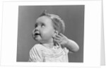 1940s 1950s close-up portrait of baby girl with curl on top of head looking to side with hand held up beside ear by Anonymous