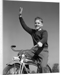 1940s 1950s smiling boy riding bike waving arm in air by Anonymous