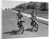 1950s teen boy girl couple riding bikes down residential street by Anonymous