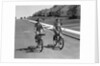 1950s teen boy girl couple riding bikes down residential street by Anonymous
