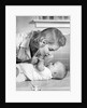 1950s mother woman bending over baby lying on layette holding hands talking by Anonymous