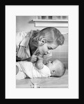 1950s mother woman bending over baby lying on layette holding hands talking by Anonymous