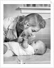 1950s mother woman bending over baby lying on layette holding hands talking by Anonymous