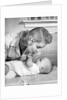 1950s mother woman bending over baby lying on layette holding hands talking by Anonymous