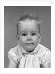 1960s head on portrait of baby girl in ruffled dress straight up hair looking at camera by Anonymous