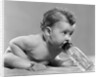 1950s baby sitting leaning forward drinking from bottle studio indoor by Anonymous