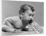 1950s baby sitting leaning forward drinking from bottle studio indoor by Anonymous