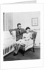 1930s 1940s mother sitting in chair in nursery baby 11 months on lap drinking from bottle father looking on leaning on crib by Anonymous