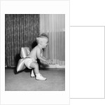 1950s laughing baby in diaper and shoes learning to walk with a pillow tied to his rear end by Anonymous