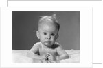1960s portrait baby lying on stomach with messy hair and bulging eyes looking at camera by Anonymous