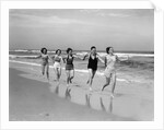 1930s four women and one man running on beach holding hands by Anonymous