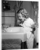 1950s little blond girl in pajamas standing at bathroom sink brushing her teeth toothpaste and toothbrush in hand by Anonymous