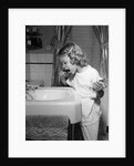 1950s little blond girl in pajamas standing at bathroom sink brushing her teeth toothpaste and toothbrush in hand by Anonymous