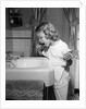 1950s little blond girl in pajamas standing at bathroom sink brushing her teeth toothpaste and toothbrush in hand by Anonymous