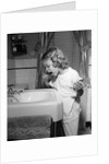 1950s little blond girl in pajamas standing at bathroom sink brushing her teeth toothpaste and toothbrush in hand by Anonymous