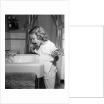1950s little blond girl in pajamas standing at bathroom sink brushing her teeth toothpaste and toothbrush in hand by Anonymous