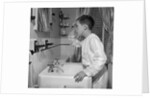 1950s boy combing hair looking in bathroom sink mirror by Anonymous