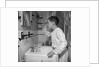 1950s boy combing hair looking in bathroom sink mirror by Anonymous