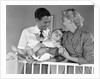 1950s smiling parents picking baby up out of crib by Anonymous