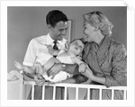 1950s smiling parents picking baby up out of crib by Anonymous