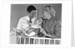 1950s smiling parents picking baby up out of crib by Anonymous