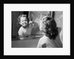 1950s girl looking in bathroom mirror brushing teeth by Anonymous