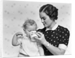 1930s woman mother giving baby daughter drink from mug by Anonymous