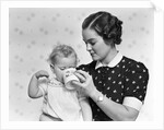 1930s woman mother giving baby daughter drink from mug by Anonymous