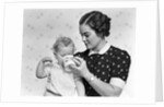 1930s woman mother giving baby daughter drink from mug by Anonymous