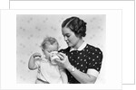 1930s woman mother giving baby daughter drink from mug by Anonymous