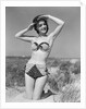 1950s smiling young woman kneeling in grassy sand wearing polka dot bikini shading eyes from sun by Anonymous