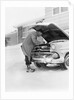 1950s man winter driveway trying to start fix car hood up by Anonymous